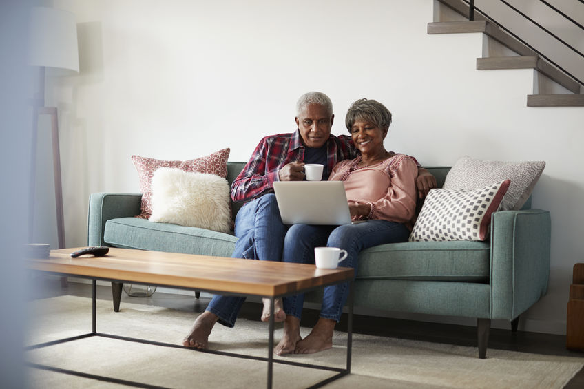 Senior couple relaxing on couch using laptop checking the veterans wartime benefits program in kentucky for the husband.