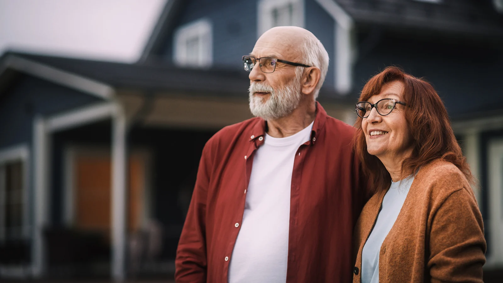 Smiling seniors standing outside their house
