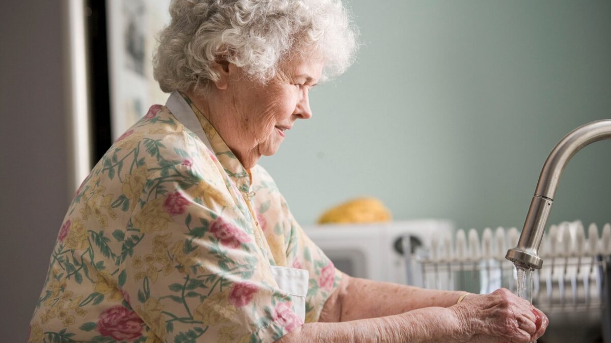 Elderly woman washing vegetables at kitchen sink
