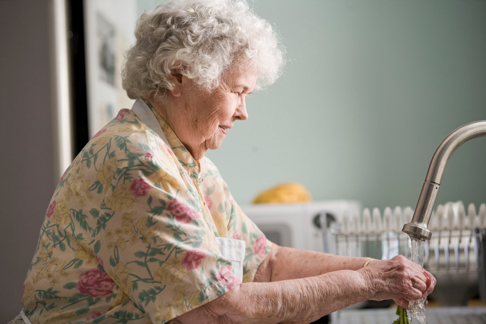 Elderly woman washing vegetables at kitchen sink