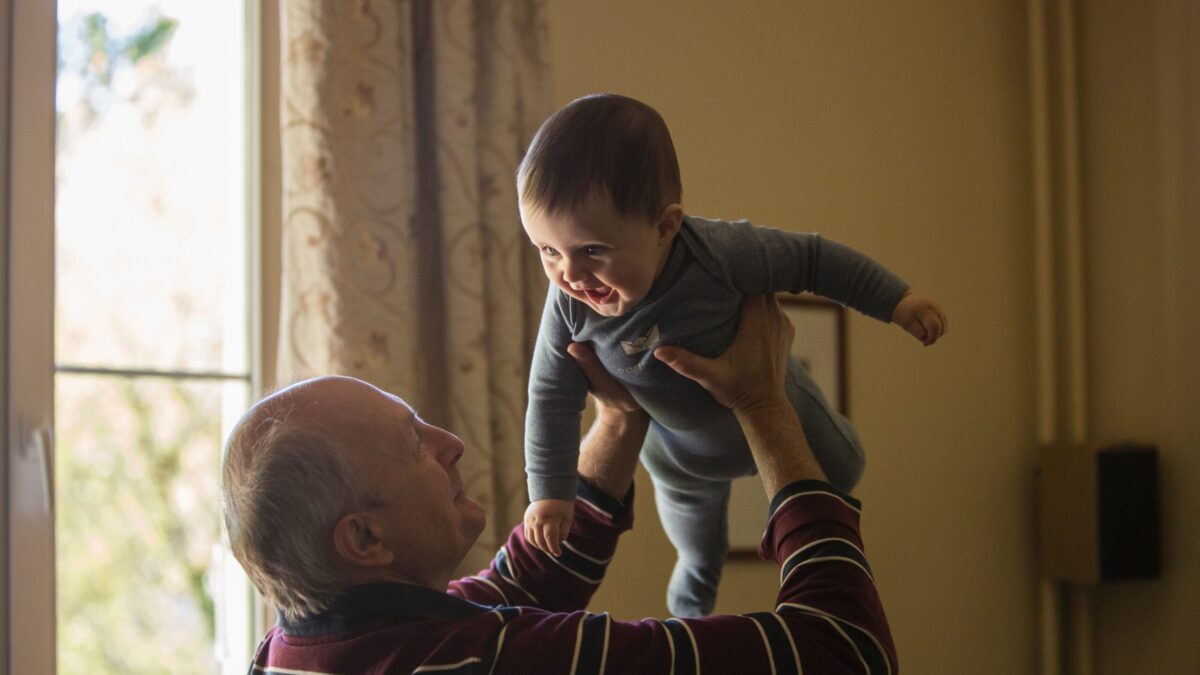 Smiling elderly man lifting happy baby indoors