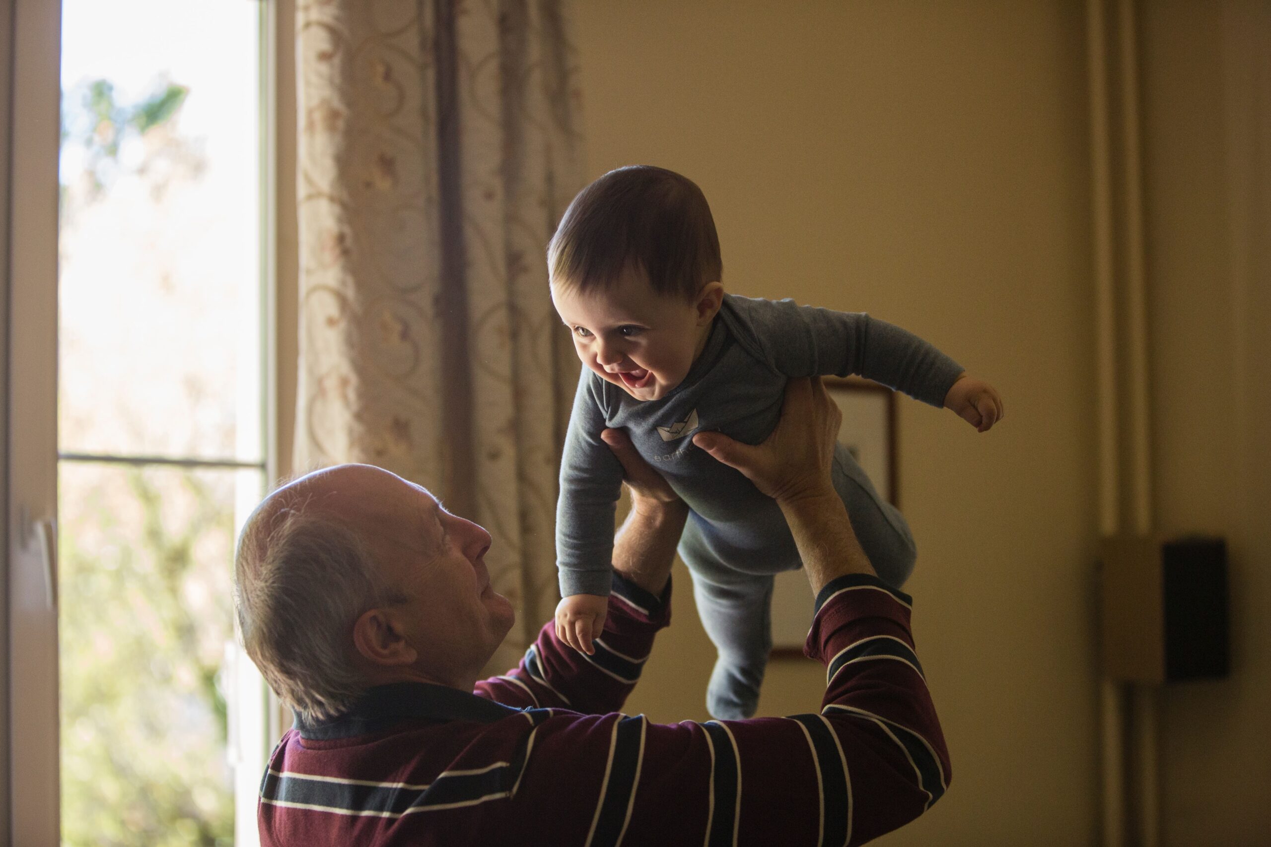 Smiling elderly man lifting happy baby indoors