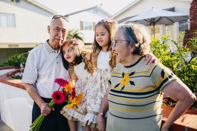 Grandparents smiling with grandchildren outdoors holding flowers